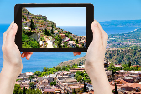 travel concept - tourist taking photo town Taormina from Castelmola, Sicily, Italy of on mobile gadgetの写真素材