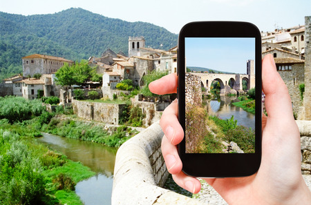 travel concept - tourist takes picture of 12th-century Romanesque bridge over the Fluvia river in Besalu town on smartphone, Spainの写真素材