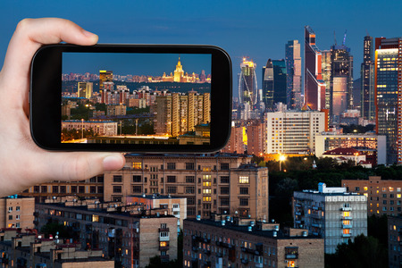 travel concept - tourist takes picture of panorama of Moscow city in blue summer night on smartphone,の写真素材