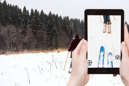 travel concept - tourist takes picture of wide cross-country skis and ski run in snow on smartphone,の写真素材