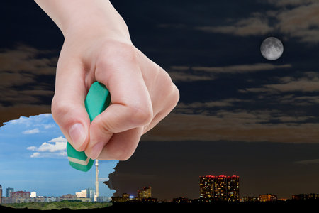 weather concept - hand deletes night cityscape by rubber eraser from image and daily urban landscape...