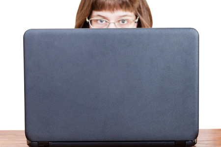 girl with glasses looks over cover of open laptopの写真素材
