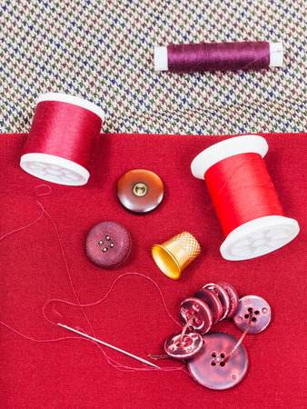 dressmaking still life - top view of bobbins with sewing thread, buttons, thimble, needle on red clothの写真素材