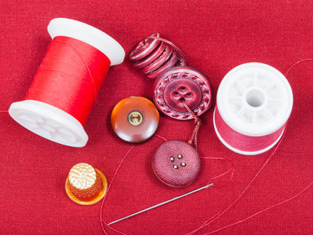 dressmaking still life - top view of bobbins with sewing thread, buttons, thimble, needle on red...