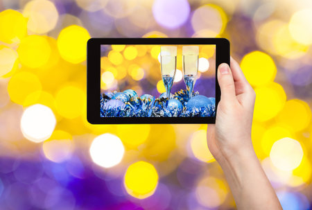 man takes photo of Christmas still life - two glasses of champagne at blue Xmas decorations with yellow and violet blurred Christmas lights bokeh backgroundの写真素材