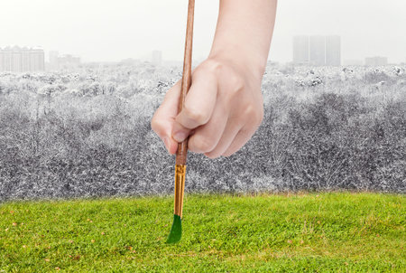 nature concept - seasons and weather changing: hand with paintbrush paints green meadow instead of winter forestの写真素材