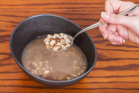 hand holds tablespoon with beans soup over ceramic bowl on wooden tableの写真素材