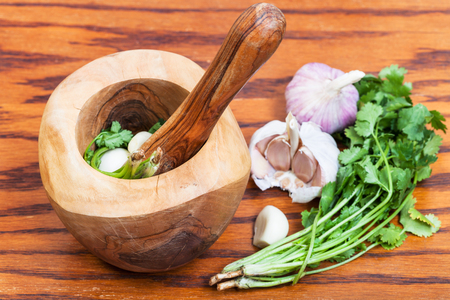 cooking seasonings - wooden mortar with cilantro grass and garlic on tableの写真素材