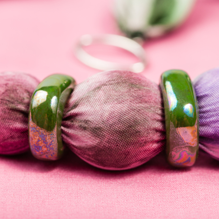 detail of handmade textile necklace - violet painted silk batik bead and green ceramic rings close up on pink backgroundの写真素材
