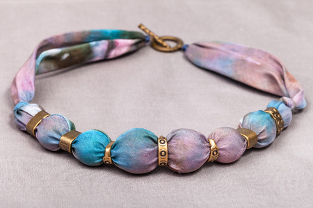 textile necklace from pink and blue painted silk and bronze beads on gray backgroundの写真素材