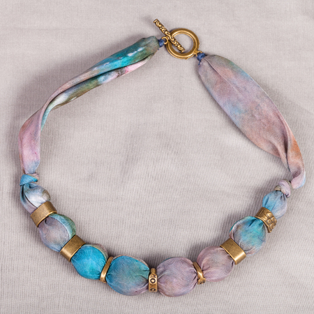 top view of textile necklace from pink and blue painted silk and bronze beads on gray backgroundの写真素材