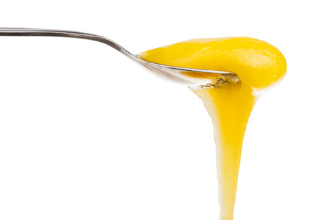 yellow dense honey flow? down from metal spoon close up isolated on white backgroundの写真素材