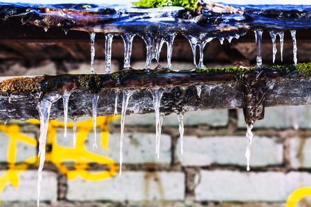 icicles on old gully of house with brick wall in sunny winter dayの写真素材