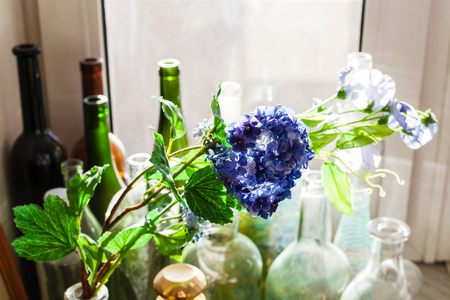 still life - textile artificial flower and old bottles covered with dust on window sill illuminated by sunlightの写真素材