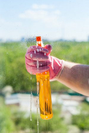 washing home window - washer sprays liquid from spray bottle to window pane with green park outside in sunny spring dayの写真素材