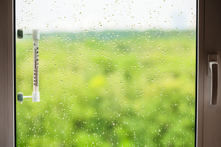 home window with rain drops and thermometer in summer dayの写真素材