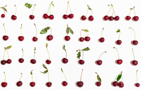 many ripe red cherries with green leaves arranged on white backgroundの写真素材
