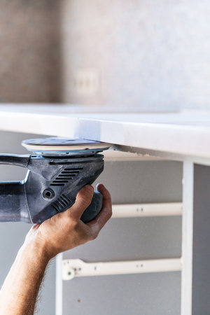 installing new tabletop on kitchen - worker polishing countertop from artificial stone by random orbital sanderの写真素材