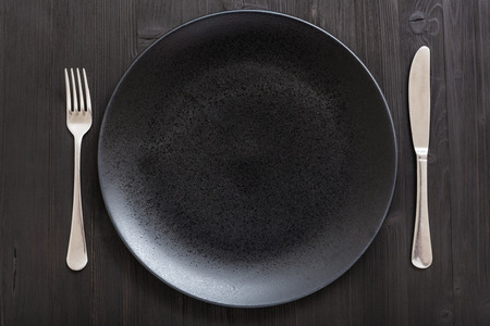 food concept - top view of black plate with knife, spoon on dark brown tableの写真素材