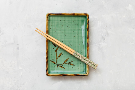 top view of green plate with chopsticks on gray concrete surfaceの写真素材