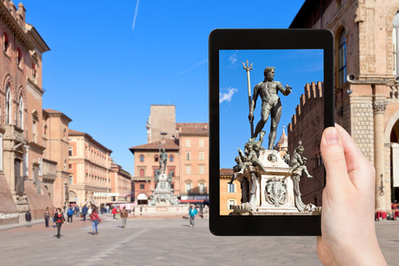 travel concept - tourist photographs fountain of Neptune in Bologna city on tablet in Italyの写真素材