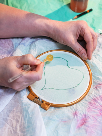 batik painting workshop - artist draws contour of heart on batik on white silk canvas clamped in the hoopの写真素材