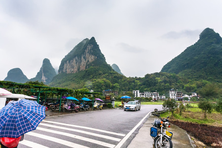 YANGSHUO, CHINA - MARCH 29, 2017: car and scooter parking lots near gate to village in Yangshuo county. Town is resort destination for domestic and foreign tourists because of scenic karst peaksのeditorial素材