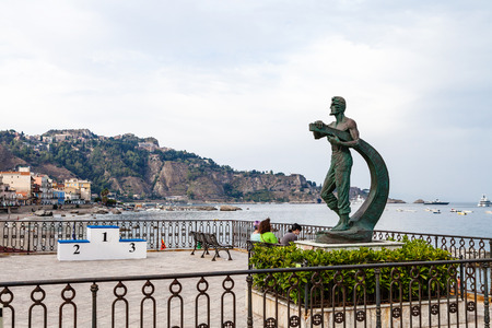 GIARDINI NAXOS, ITALY - JUNE 28, 2017: tourists near statue L' Uomo e il Mare (Man and the Sea) on waterfront in Giardini-Naxos. Giardini Naxos is seaside resort on Ionian Sea coast since the 1970sのeditorial素材