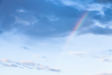 rainbow under rainy clouds in blue evening sky in summerの写真素材