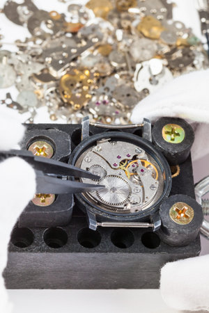 watchmaker workshop - repairing of mechanical watch by tweezers with spare parts on white background
