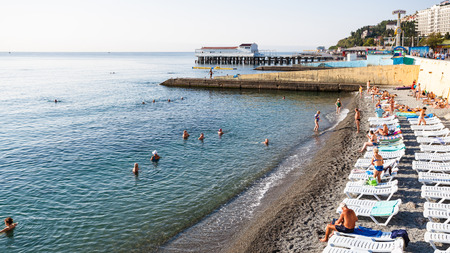 ALUSHTA, CRIMEA - SEPTEMBER 21, 2017: tourists and loungers on urban pebble beach on coast of Black Sea in Alushta in morning. Alushta is seaside resort town on southern coast of the Crimean peninsulaのeditorial素材
