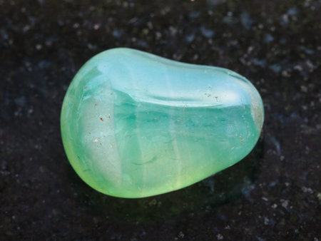 macro shooting of natural mineral rock specimen - tumbled green Calcite gemstone on dark granite...