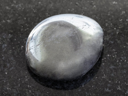 macro shooting of natural mineral rock specimen - tumbled hematite gemstone on dark granite...