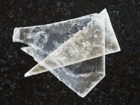 macro shooting of natural mineral rock specimen - raw muscovite mica lamina on dark granite...