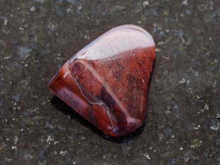 macro shooting of natural mineral rock specimen - polished jaspilite jasper gemstone on dark granite backgroundの写真素材