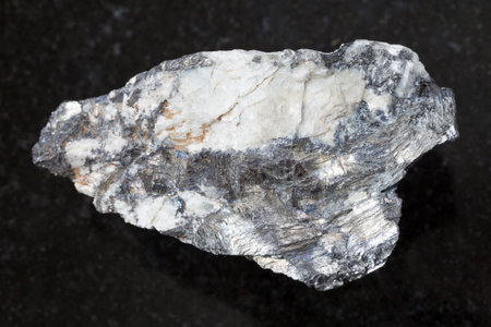 macro shooting of natural mineral rock specimen - native Bismuthinite in raw quartz stone on dark...