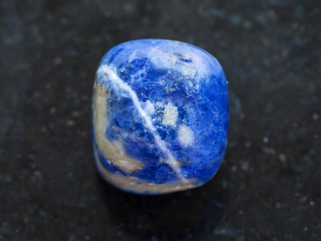 macro shooting of natural mineral rock specimen - tumbled Sodalite gemstone on dark granite backgroundの写真素材