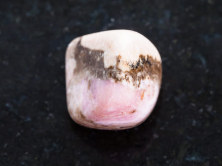 macro shooting of natural mineral rock specimen - tumbled Rhodochrosite gemstone on dark granite...