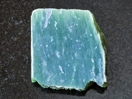 macro shooting of natural mineral rock specimen - raw nephrite stone slab on dark granite background