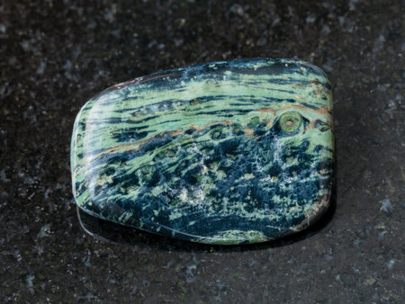 macro shooting of natural mineral rock specimen - tumbled rhyolite gemstone on dark granite...