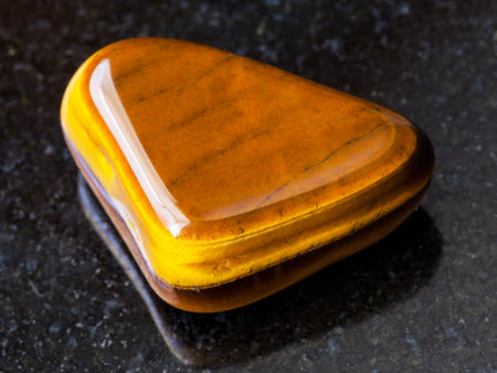 macro shooting of natural mineral rock specimen - polished tiger-eye gem stone on dark granite...