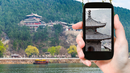 travel concept - tourist photographs pagoda on East Hill of Chinese Buddhist monument Longmen Grottoes in spring on smartphoneの写真素材