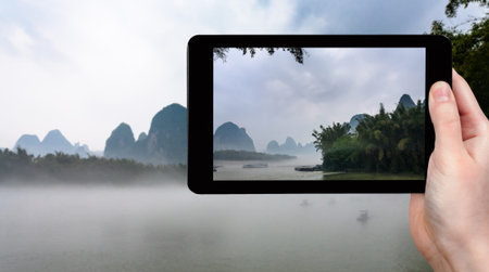 travel concept - tourist photographs fog over river near Xingping town in Yangshuo county in spring...