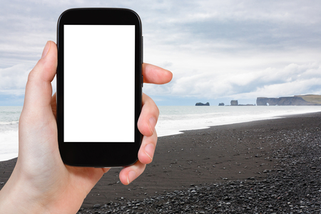 travel concept - tourist photographs Reynisfjara Beach and view of Dyrholaey promontory in Iceland on Atlantic South Coast in autumn on smartphone with cut out screen for advertising logoの写真素材