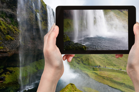 travel concept - tourist photographs Seljalandsfoss waterfall of Seljalands River in Katla Geopark on Icelandic Atlantic South Coast in Iceland in september on tabletの写真素材
