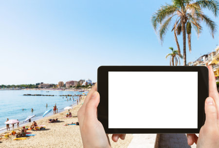 travel concept - tourist photographs urban sand beach in Giardini-Naxos town in Sicily Italy in...