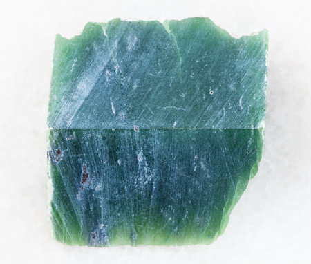 macro shooting of natural mineral rock specimen - raw nephrite stone slab on white marble background