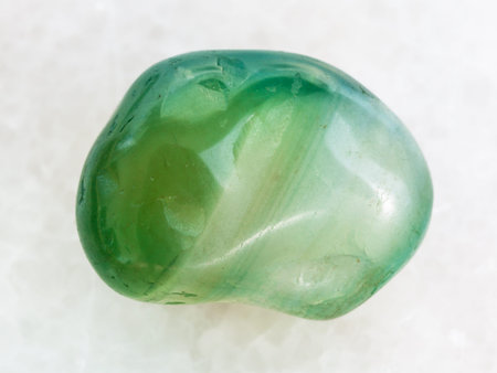 macro shooting of natural mineral rock specimen - polished green dyed agate gemstone on white marble...