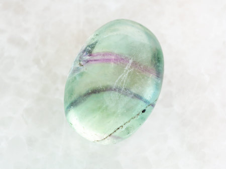 macro shooting of natural mineral rock specimen - tumbled Fluorite gemstone on white marble...