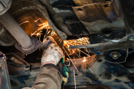 repairing of corrugation muffler of exhaust system in car workshop - mechanic cleans the muffler pipe on car by angle grinderの写真素材